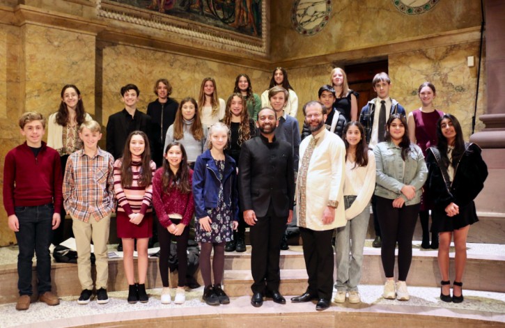 Sameer Patel, conductor, and William Harvey, composer and violinist, surrounded by multiple middle school artists and writers participating in the Listen Up creative response program, onstage in Richardson Auditorium