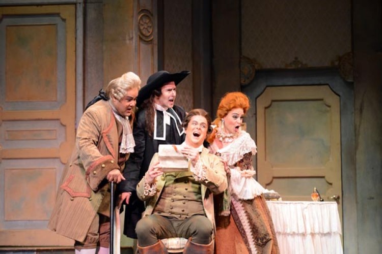 Singers in costume for an opera are clustered in the center of the image. A man is seated, holding a letter. Two men and a woman stand behind him, looking at the letter and each other.
