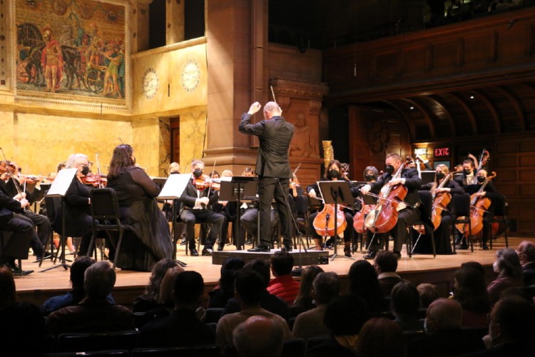 Rossen Milanov conducts the members of the Princeton Symphony Orchestra. Audience members are visible in the foreground.