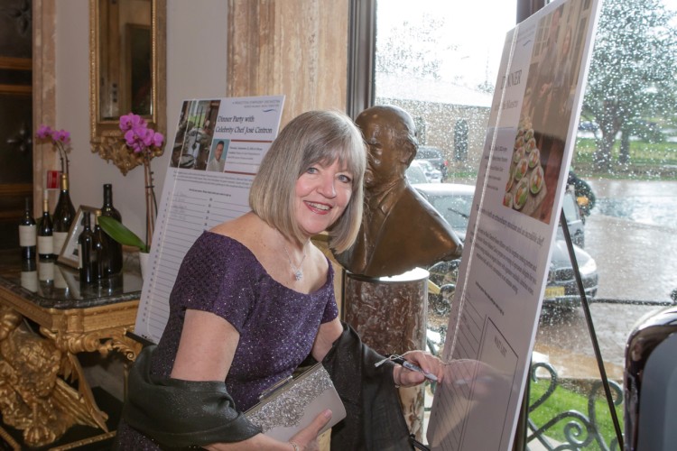 A gala attendee smiles at the camera. She is holding a pen in her left hand as she signs up for a party board.