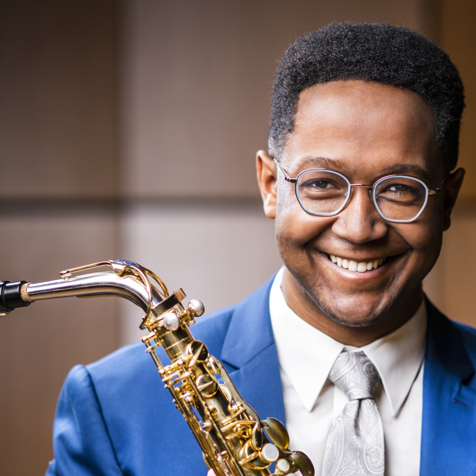Saxophonist Steven Banks holds his instrument; he wears a bright blue blazer and white collared shirt with tie.