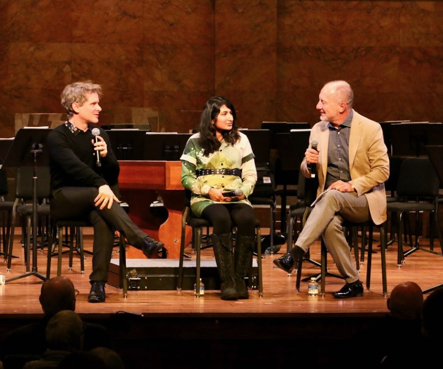Three people chat on stage in front of an audience listening in. 
