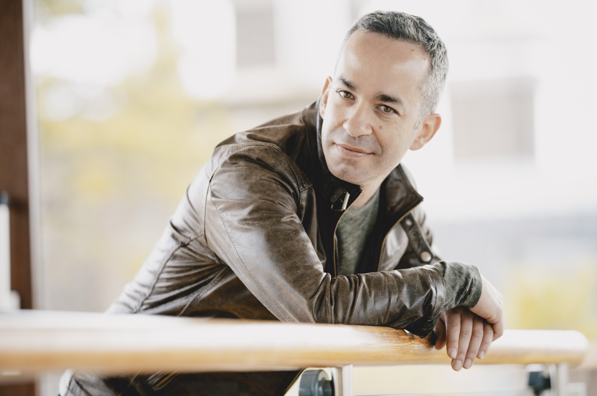 Pianist Inon Barnatan, wearing a leather jacket, leans over an outdoor railing